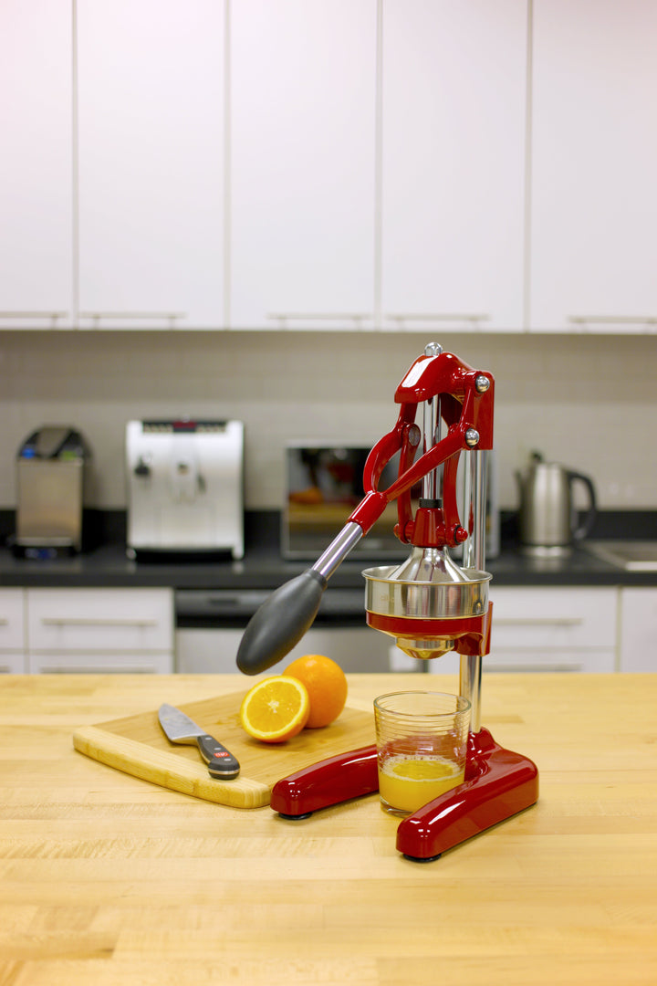 Red citrus press on countertop with juicing cup and orange halves
