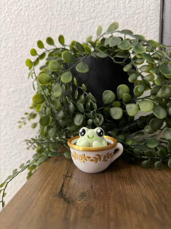 Frog toy popping from a small white teacup, orange text on cup rim
