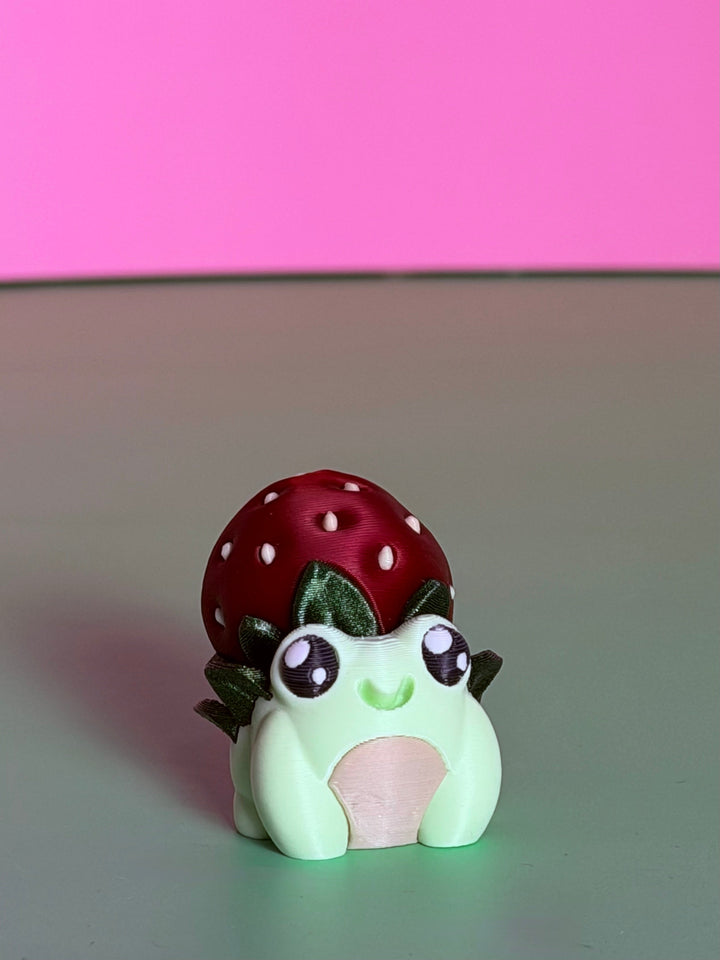 Frog toy with red strawberry cap and white dots, cute wide-eyed face
