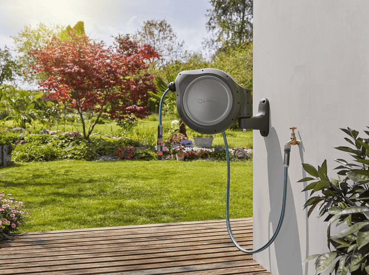 Wall-mounted retractable hose reel with gray drum and extended hose outdoors