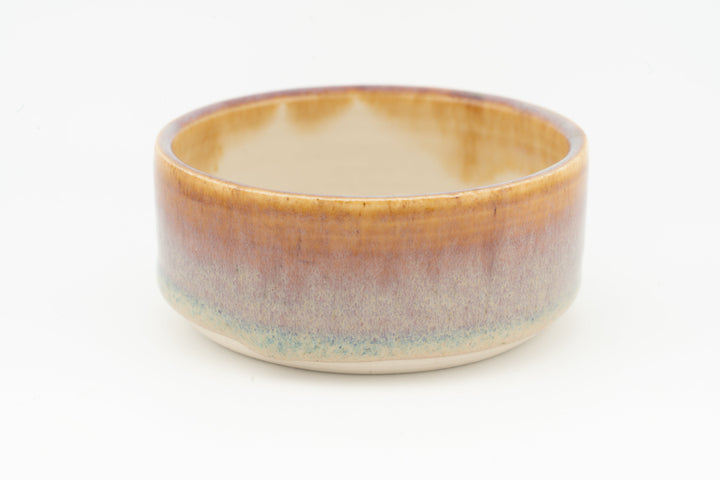 Ceramic condiment cup with warm tan interior, amber glaze outside, and teal edge