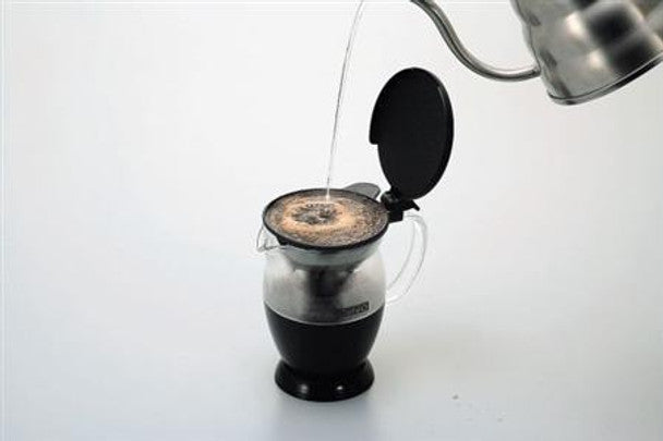 Black coffee dripper base with clear carafe as hot coffee pours into the filter