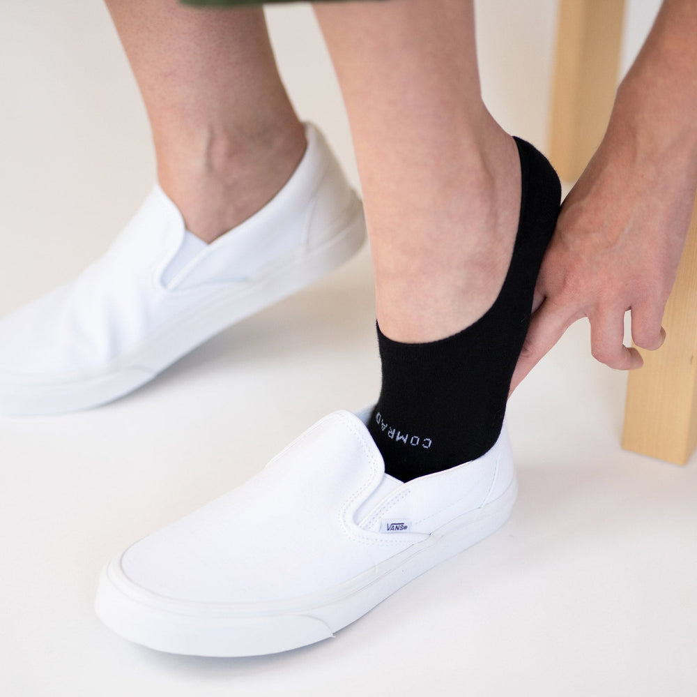Black no-show socks on feet with white sneakers, low profile ankle opening