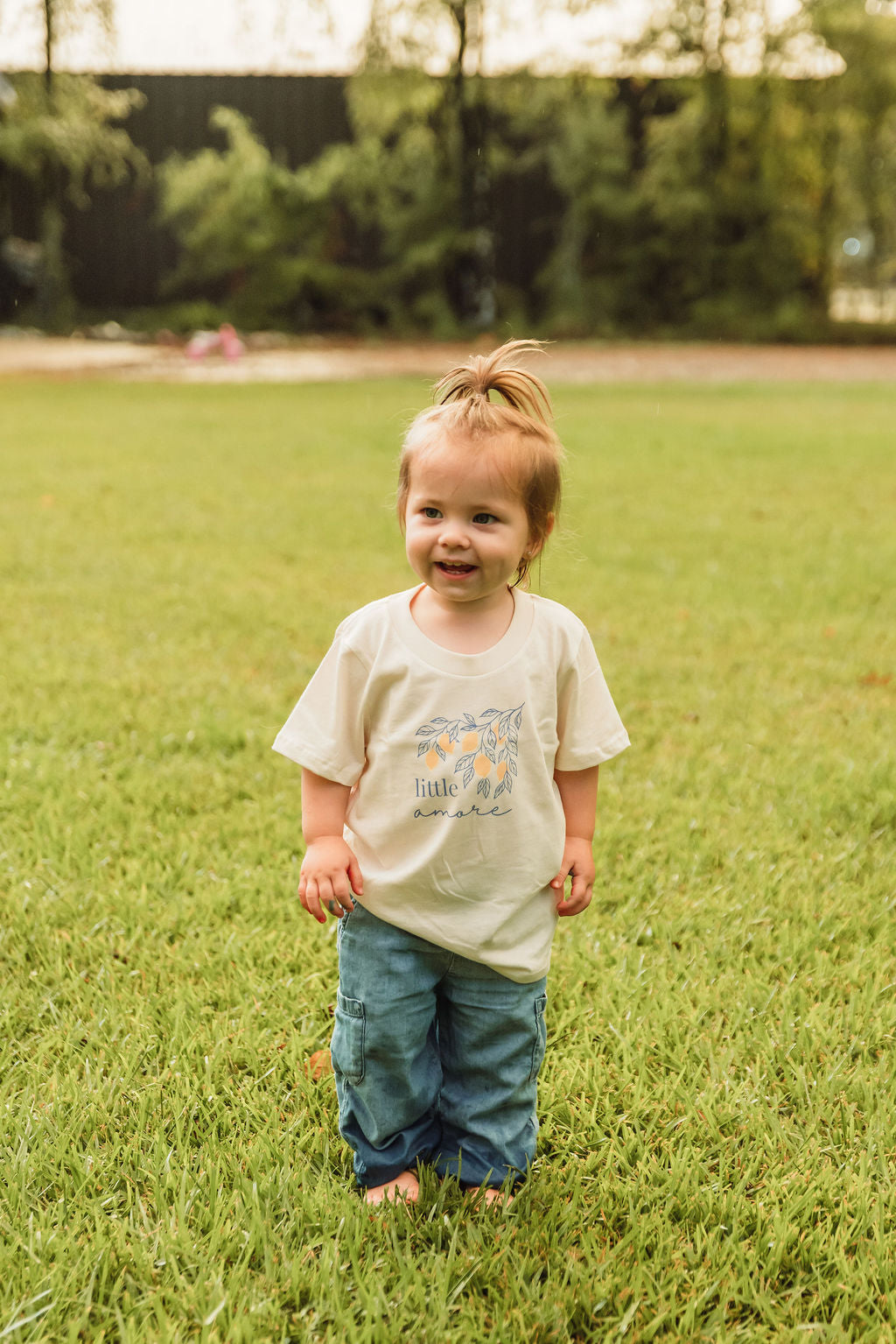 Kids organic cotton T-shirt, cream; child wearing front graphic “little amore”.