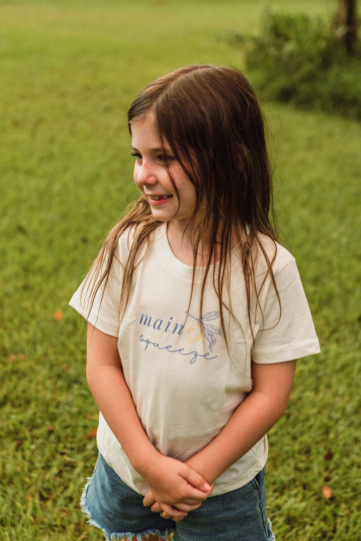 Cream organic kids t-shirt with blue 'main squeeze' leaf graphic, close-up.