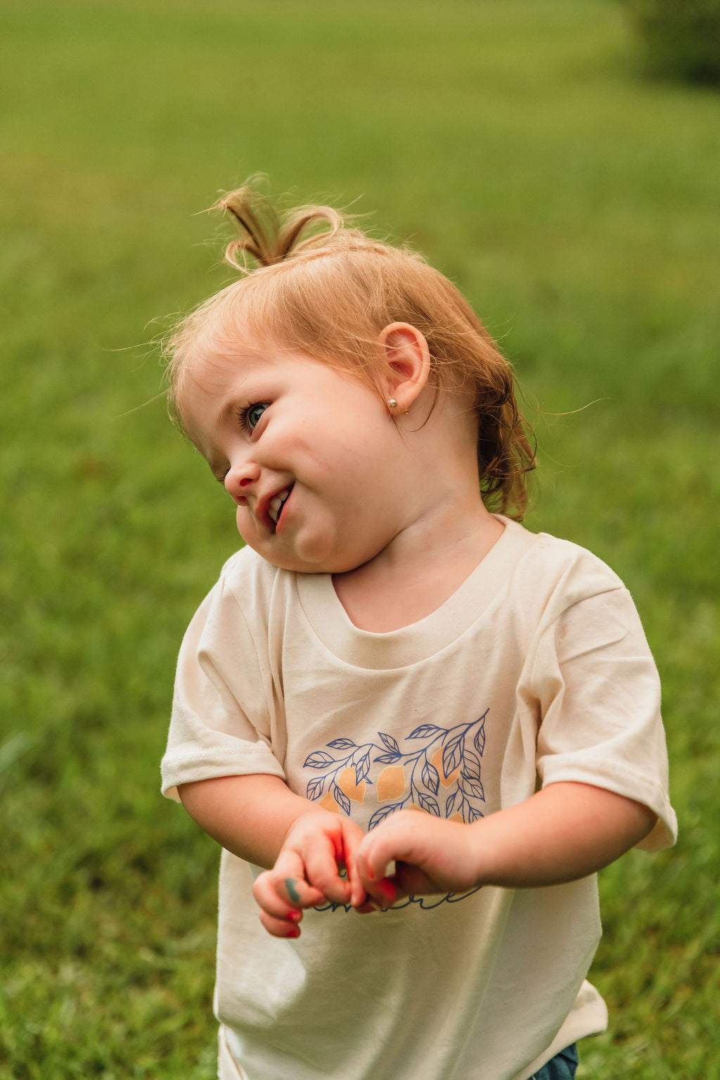 Kids organic cotton T-shirt, cream; close-up of child in “little amore” leaf graphic.