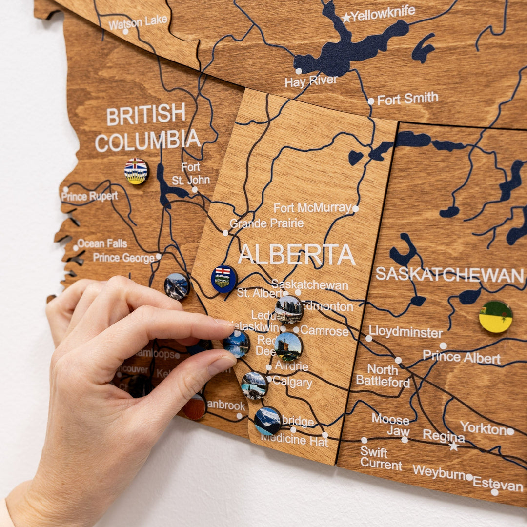 Canada landmarks pin set card held over wooden map board with labeled provinces
