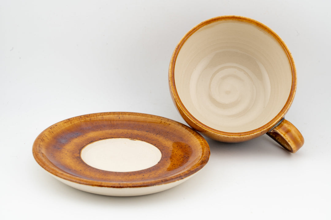 Orange-brown glazed cappuccino cup opening and matching saucer with circular pattern