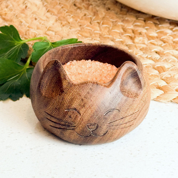 Cat-shaped wooden salt bowl with pale salt crystals, carved cat face