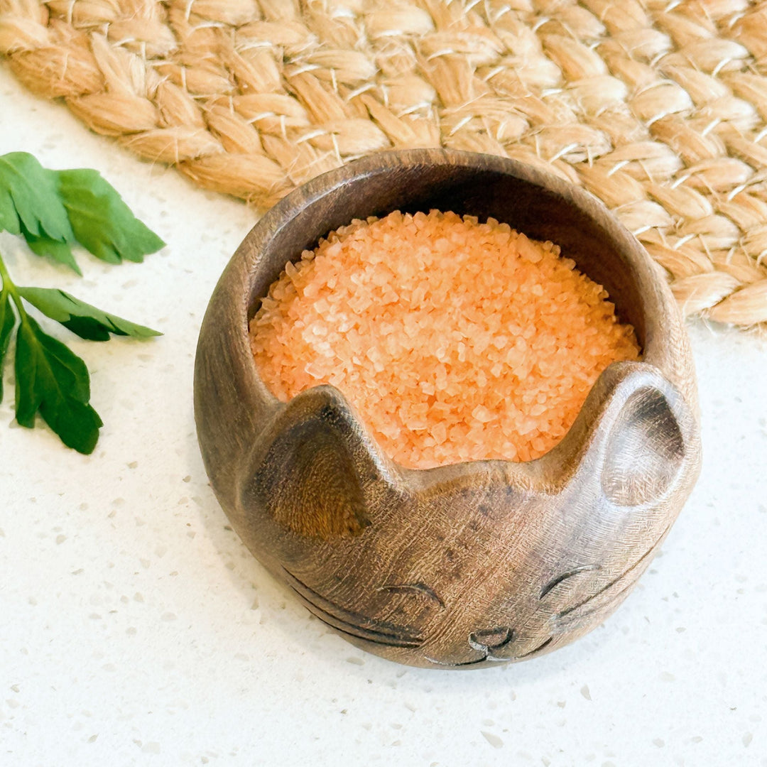 Cat-shaped wooden salt bowl filled with pink-orange salt crystals, carved cat face