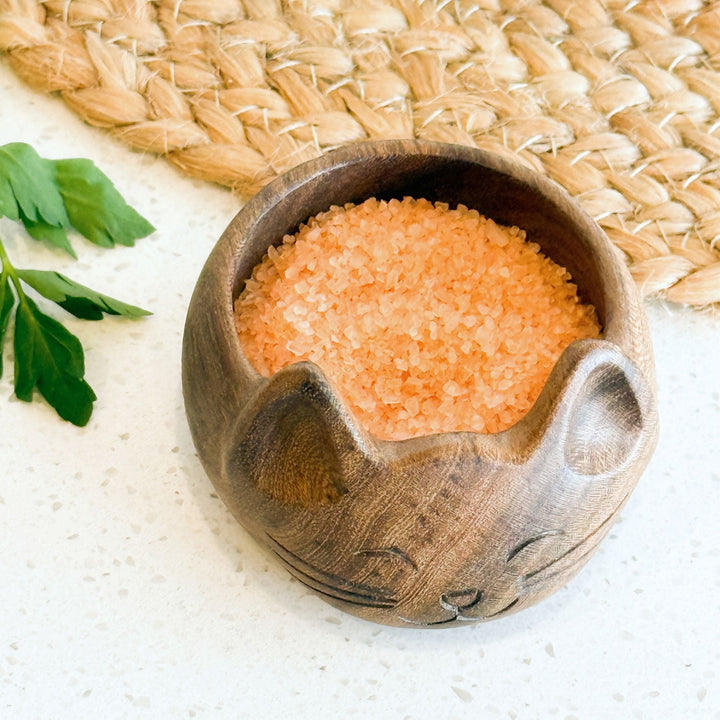 Cat-shaped wooden salt bowl filled with pink-orange salt crystals, carved cat face