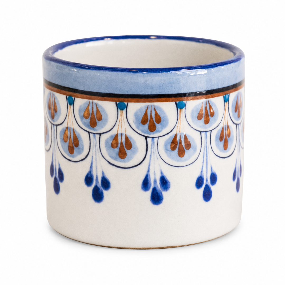 Stoneware cup close-up with orange-and-blue raindrop pattern and glossy blue rim.