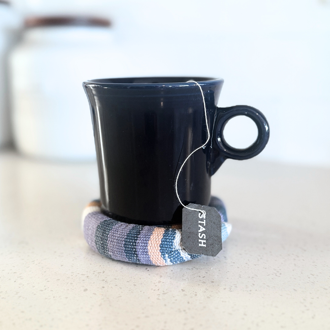 Round fabric trivet under a dark blue mug, with plaid stripe pattern and stitched rosette center