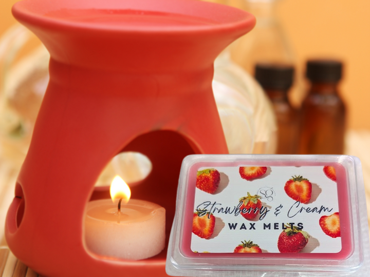 Strawberry and cream wax melt in clear clamshell beside an oil warmer flame