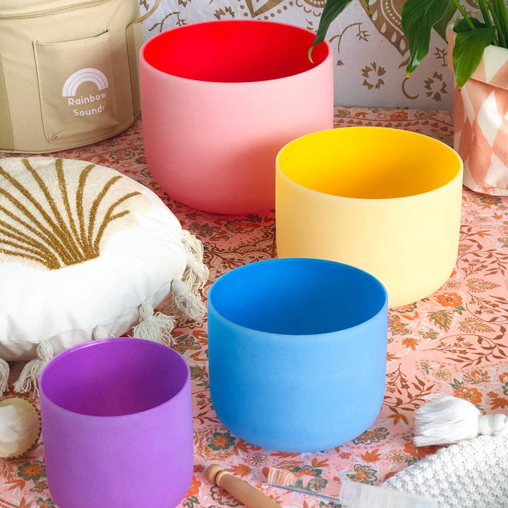 Set of 4 colorful sound bowls: red, yellow, blue, and purple beside beige case