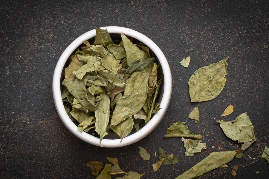 Bowl of dried curry leaves, scattered green leaf pieces