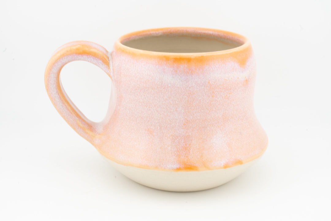 Peach-orange ceramic mug with wide handle, speckled glaze and glowing orange rim