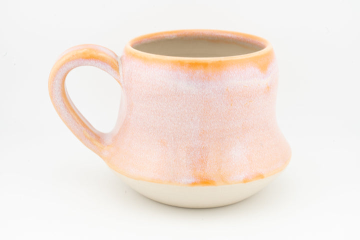 Peach-orange ceramic mug with wide handle, speckled glaze and glowing orange rim