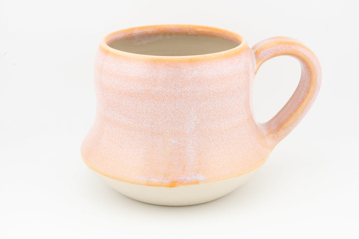 Peach-orange ceramic mug with wide handle, textured speckled glaze and cream base