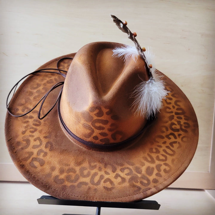 Wide-brim tan cowgirl hat with leopard print and feather hatband on top
