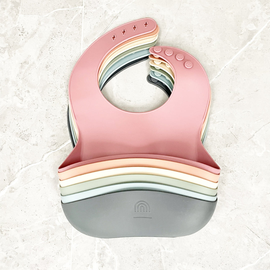 Pink and gray silicone bucket bib with stacked rainbow edge and snap buttons