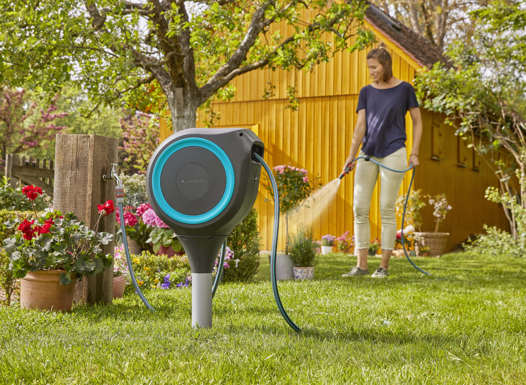 Gray roll-up garden hose reel in a garden with blue ring and connected hose line