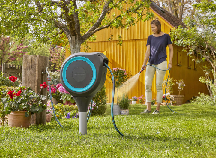 Gray roll-up garden hose reel in a garden with blue ring and connected hose line