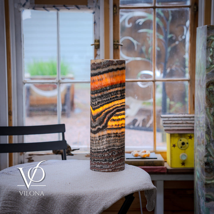 Patterned ceramic table lamp with glowing cylindrical shade in orange, black, and cream stripes
