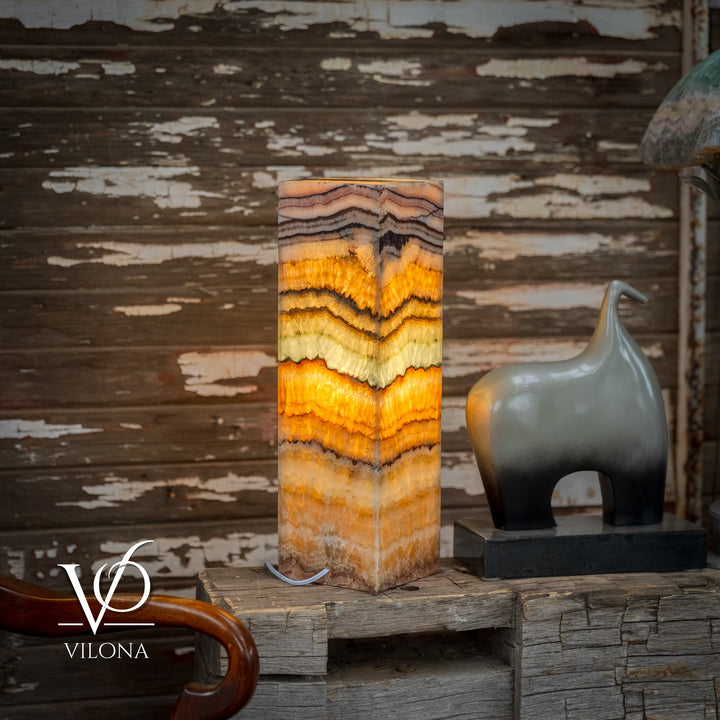 Square onyx table lamp with tall faceted stone body in gold, cream, and dark waves
