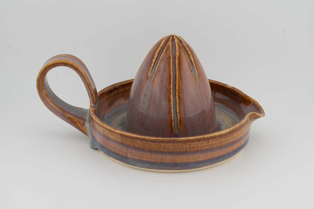 Brown ceramic citrus juicer with cone reamer and curved side handle; round drip tray.