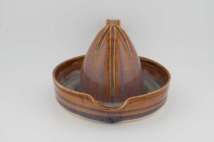 Brown ceramic citrus juicer with cone reamer centered in drip tray and wide rim.