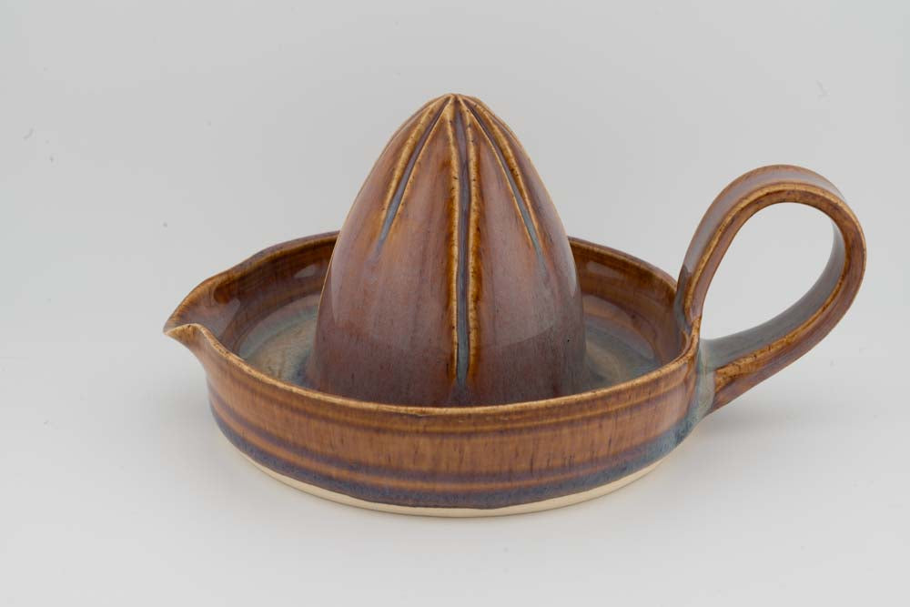 Ceramic citrus juicer with cone reamer, small spout, and side handle; brown glaze finish.
