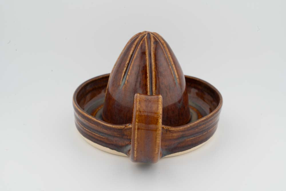 Ceramic citrus juicer with brown cone inside the tray, featuring a front pouring spout.