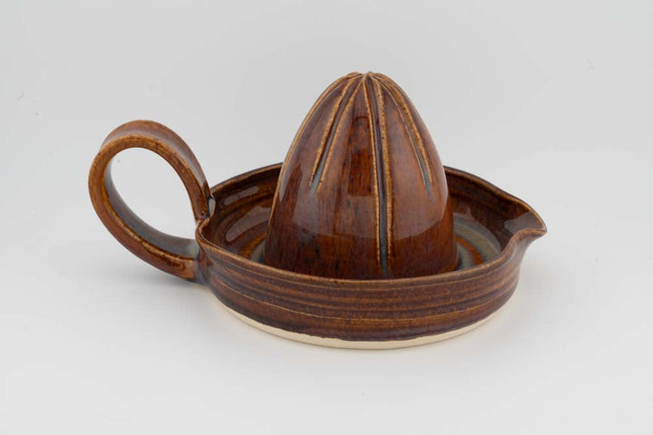 Ceramic citrus juicer with a brown cone and side handle, glazed finish.