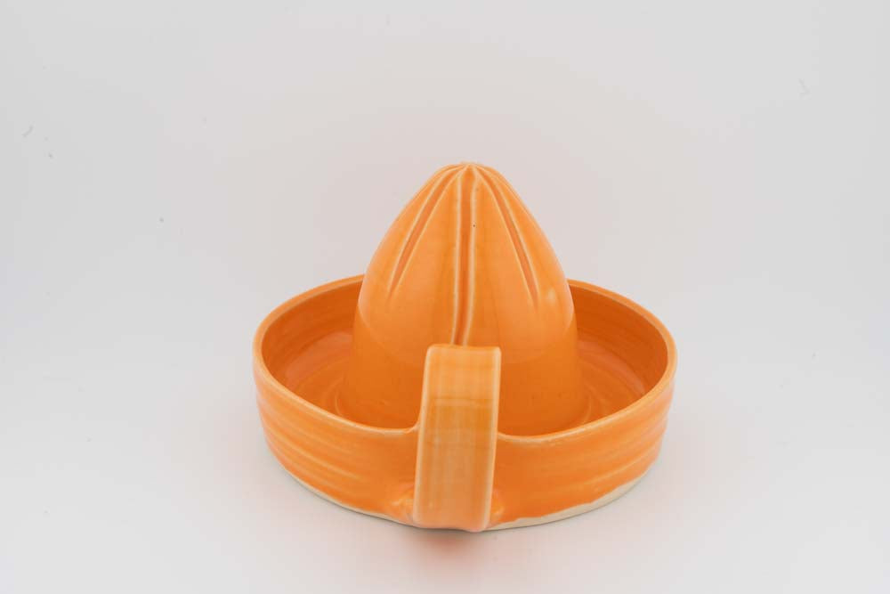 Orange ceramic citrus juicer with cone reamer and front spout on round drip tray.
