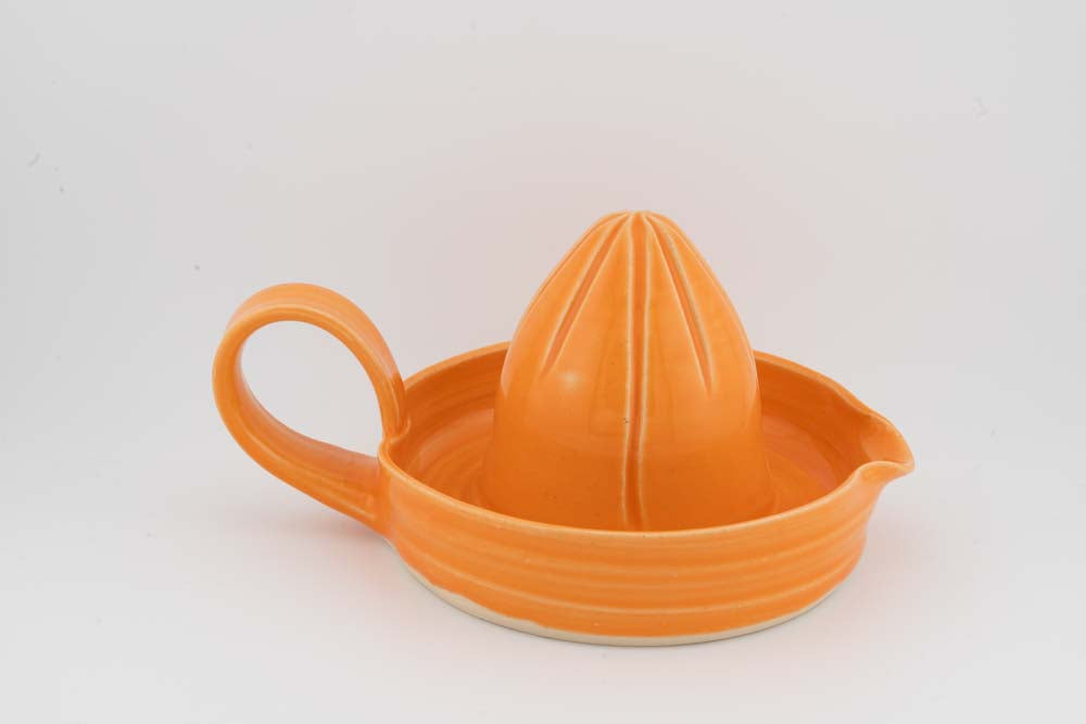 Orange ceramic citrus juicer with cone reamer, curved side handle, and wide drip tray.
