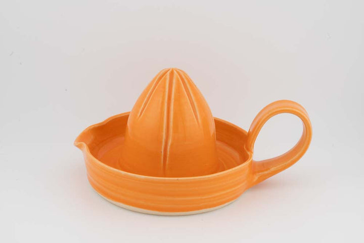 Orange ceramic citrus juicer with cone reamer, drip tray, and side handle; glossy finish.