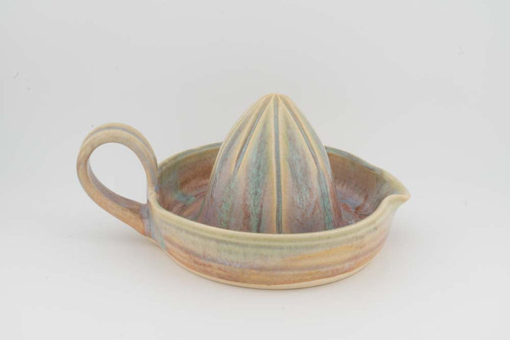 Ceramic citrus juicer with beige tray, green-brown accents, upright cone, and handle.