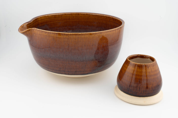 Brown ceramic matcha bowl with side spout-like lip and matching small whisk holder