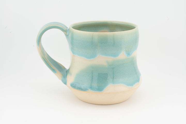 Tall ceramic mug with turquoise drip glaze and round handle, cream base