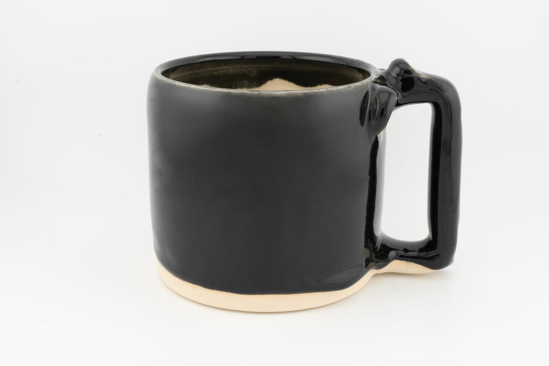 Ceramic mug with glossy black glaze, creamy base, and side handle