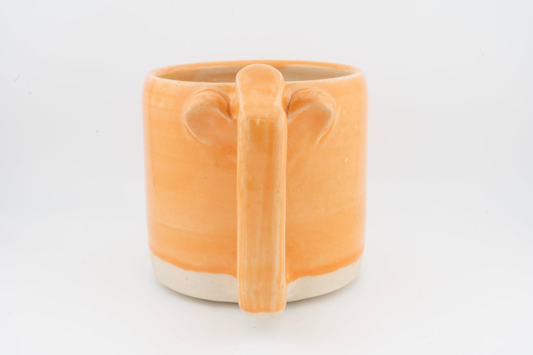 Ceramic mug with orange glaze and front handle with drip texture.