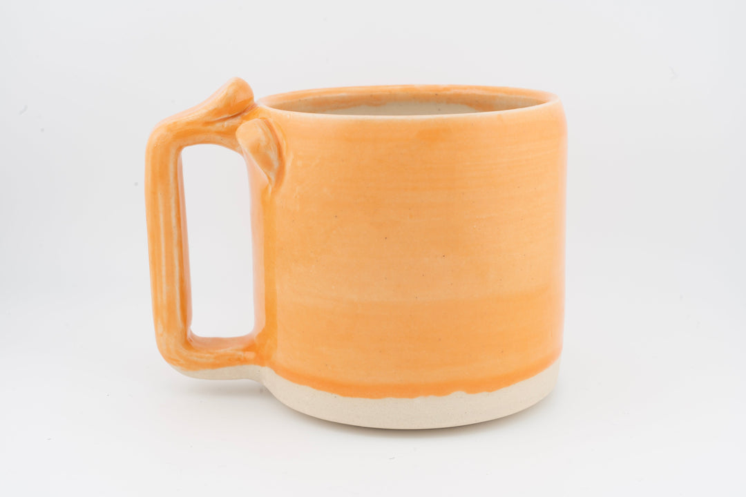 Ceramic mug with orange glaze, side handle, and white base rim.