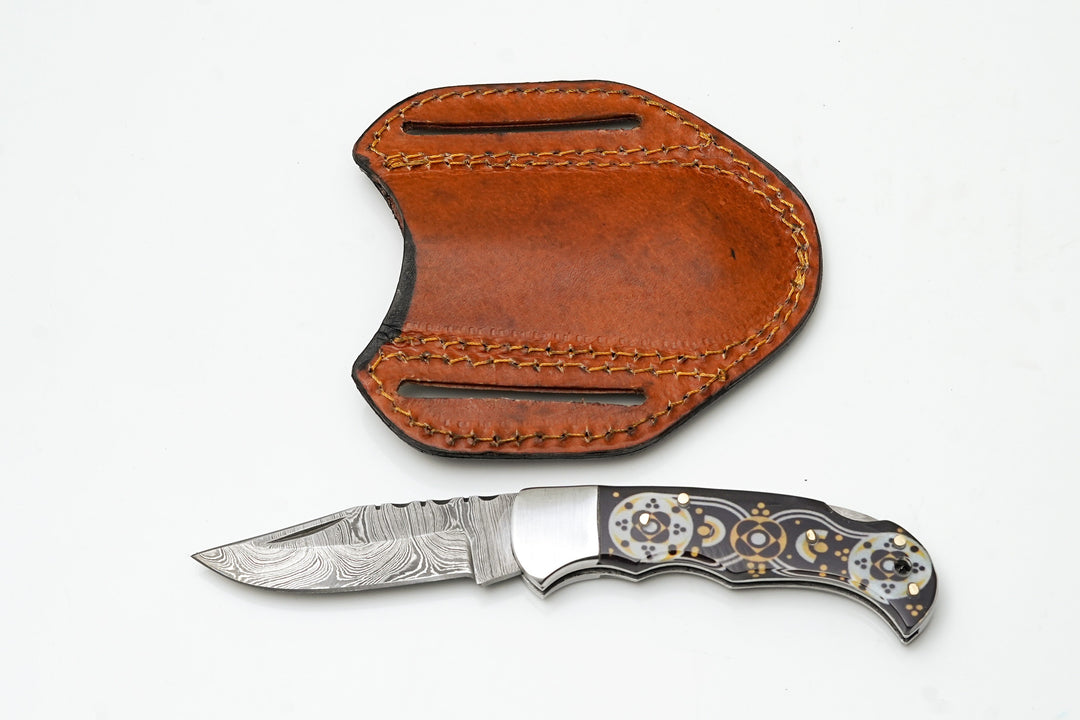 Folding knife with Damascus drop-point blade and black/gold mosaic handle, leather carry pouch