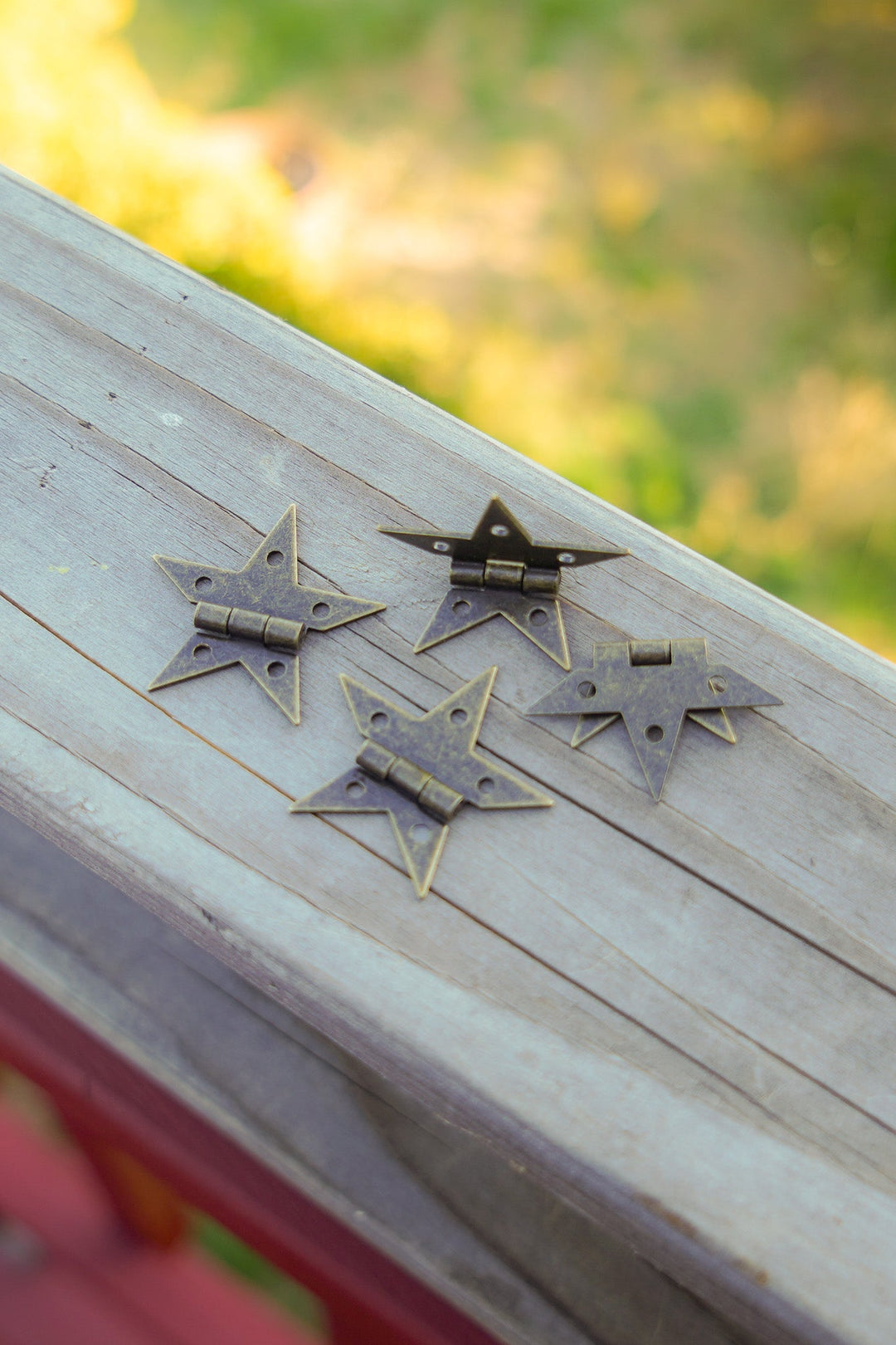 Small bronze star hinges with attached arms and screw holes on a wooden board