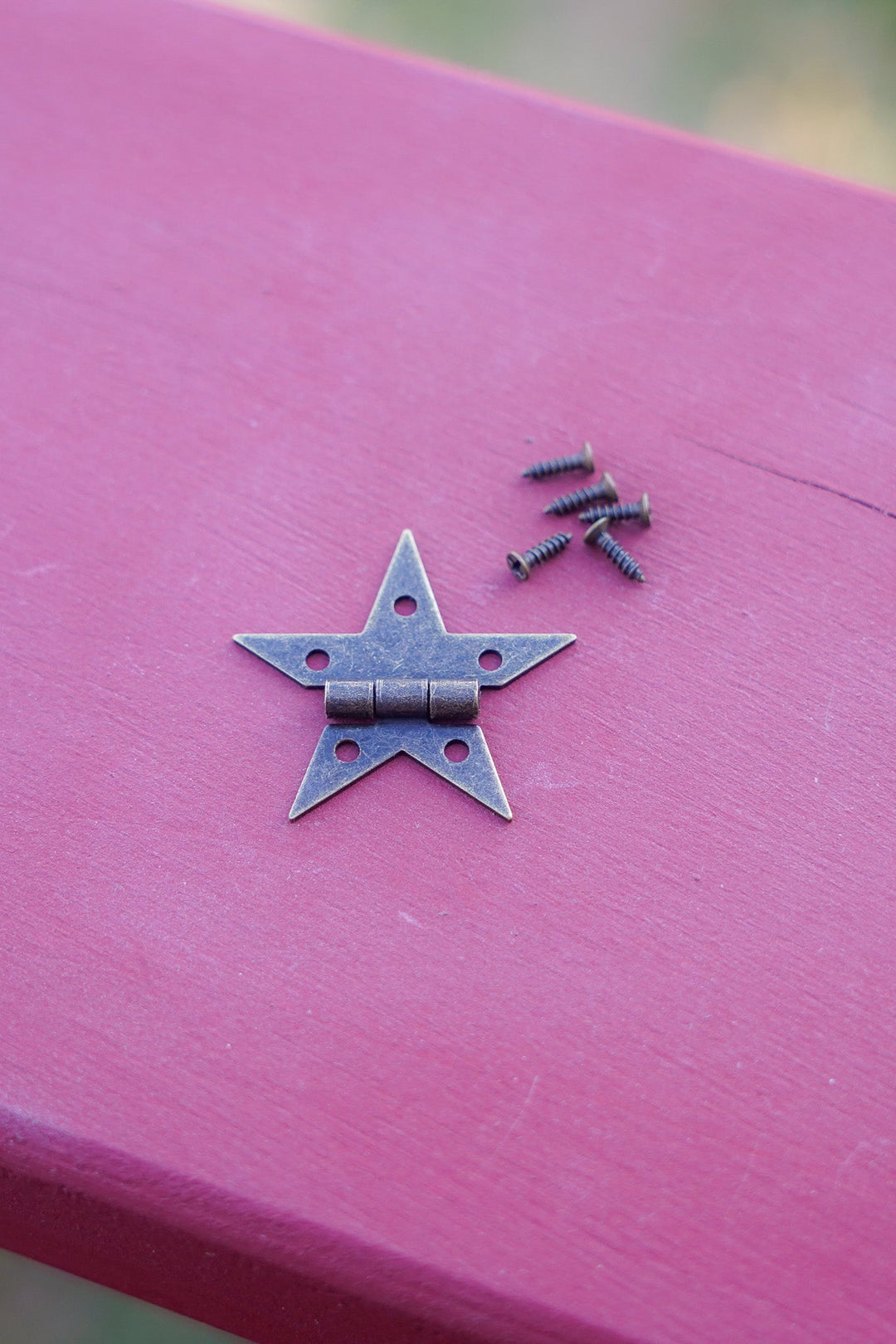Small bronze star hinge with two screws on a painted wooden surface