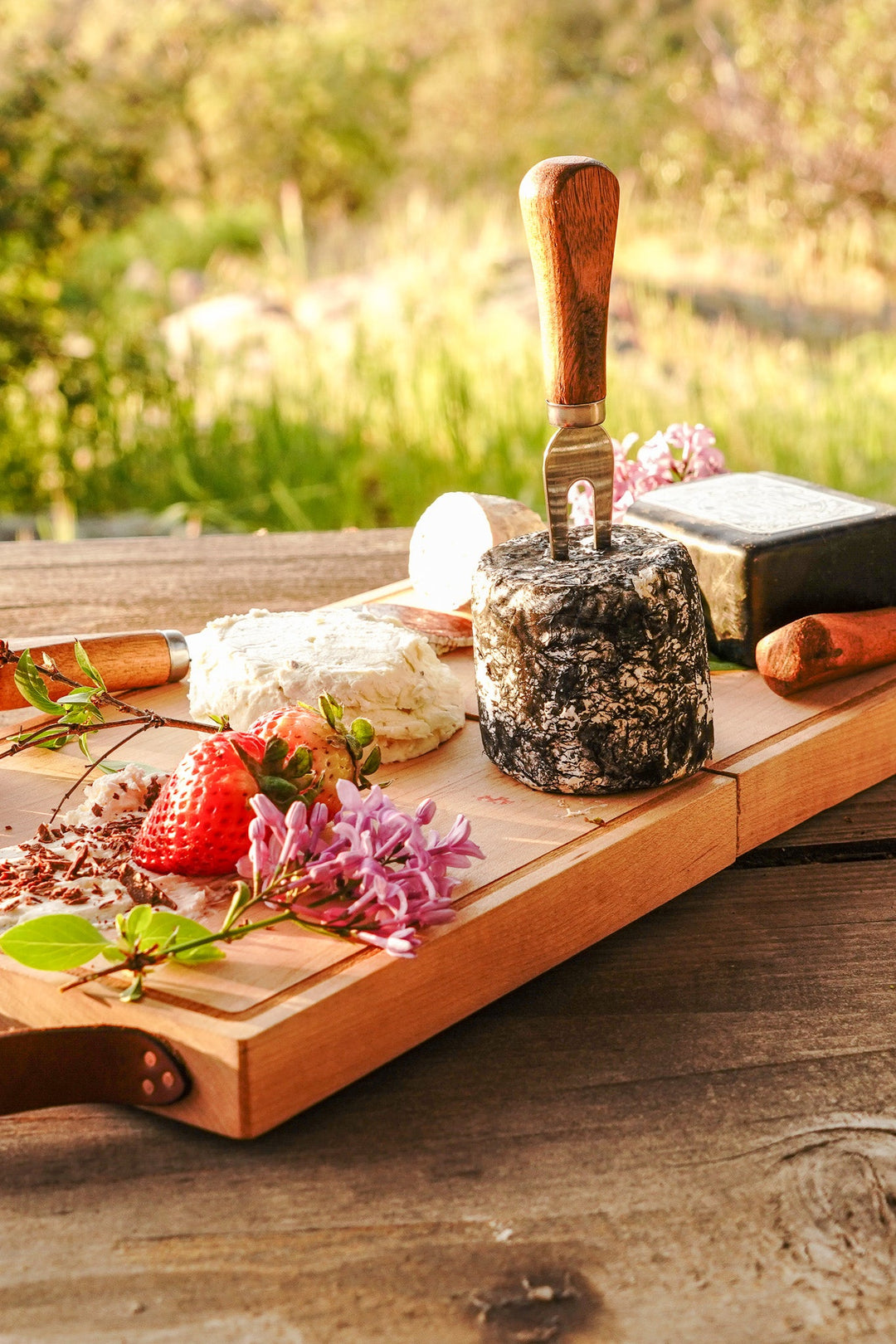 Wooden folding cheese board with handle and cheese knives on outdoor table