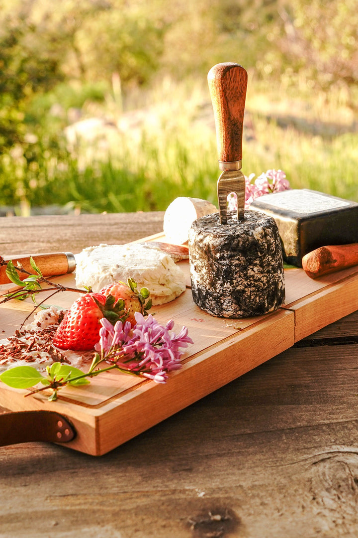 Wooden folding cheese board with handle and cheese knives on outdoor table
