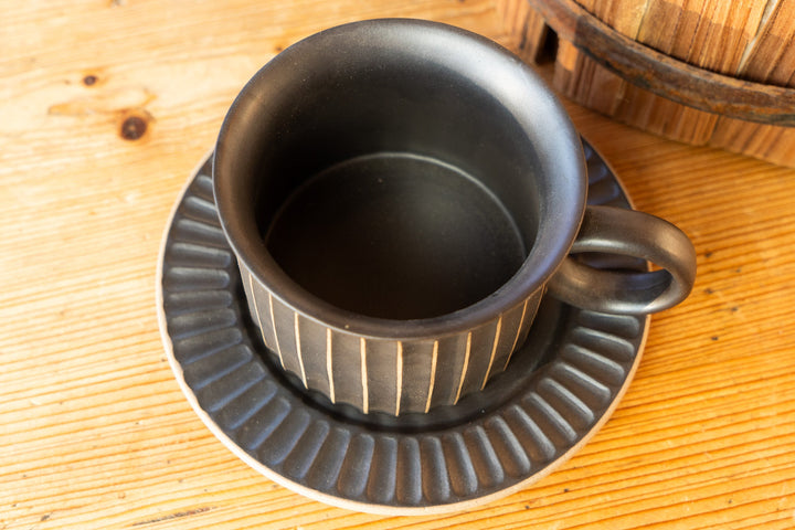Ribbed dark mug with side handle and matching ridged saucer on tabletop