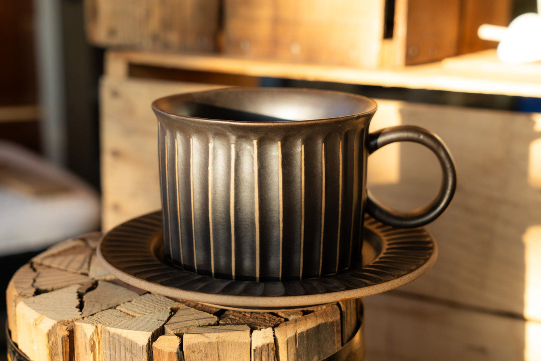 Ribbed dark coffee mug and matching saucer on wood stump, vertical stripe texture